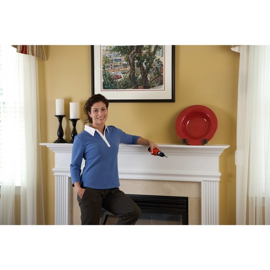 Person holding Cordless Screwdriver while leaning against a mantel shelf with a wall painting hung behind it.