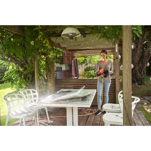 Cordless power cleaner kit being used by a person to spray water on a table in a gazebo.
