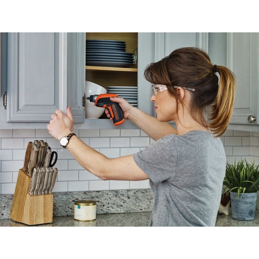 Lithium Rechargeable Screwdriver being used by person to install hinge on kitchen wooden cabinet.