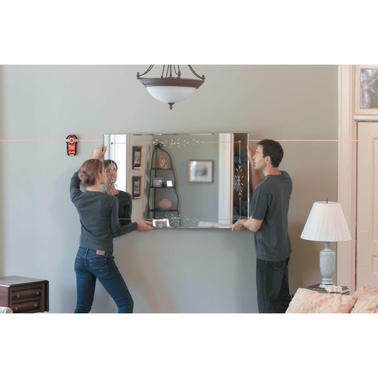 BullsEye Auto Leveling Laser with Stud Sensor being used by two persons to install mirror on wall.