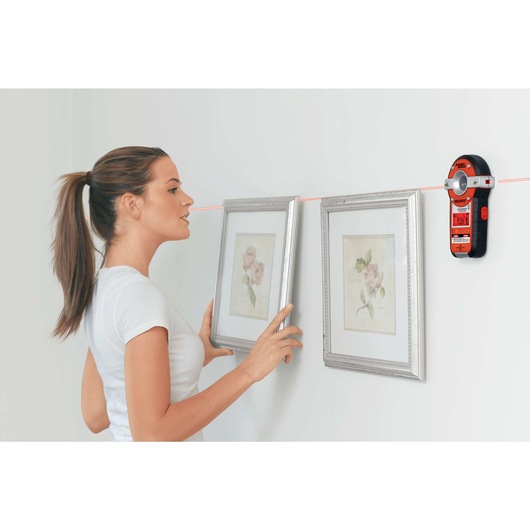 BullsEye Auto Leveling Laser with Stud Sensor being used by person for precise laser leveling to hang pictures on wall.
