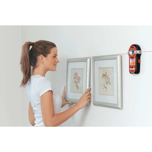 Bulls Eye Auto Leveling Laser with Stud Sensor being used by person to level paintings on wall.