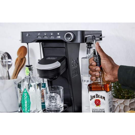 close-up, on the patio, of a man's hand loading a bottle of whiskey into the easy load liquor system on the bev by BLACK+DECKER™ cocktail maker