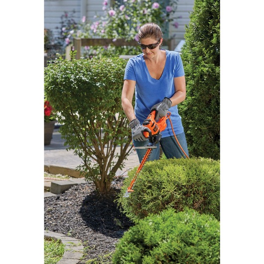16 inch SAWBLADE electric hedge trimmer being used by a person to trim hedge.