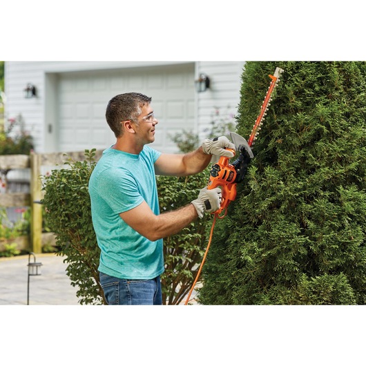 16 inch saw blade electric hedge trimmer being used to trim a tree by a person.