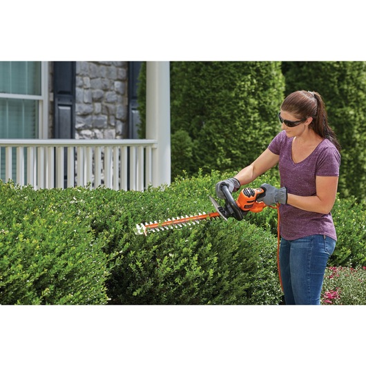 20 inch SAWBLADE electric hedge trimmer being sued by a person to trim hedge.