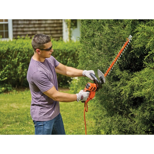 22 inch SAWBLADE electric hedge trimmer being used by a person to trim a hedge.