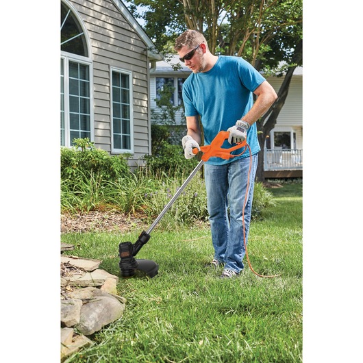 Electric string trimmer being used by a person to trim grass.
