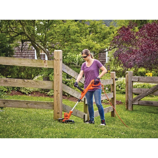 6.5 Amp 14 inch AFS electric string trimmer edger being used by a person to trim grass in hard to reach area.