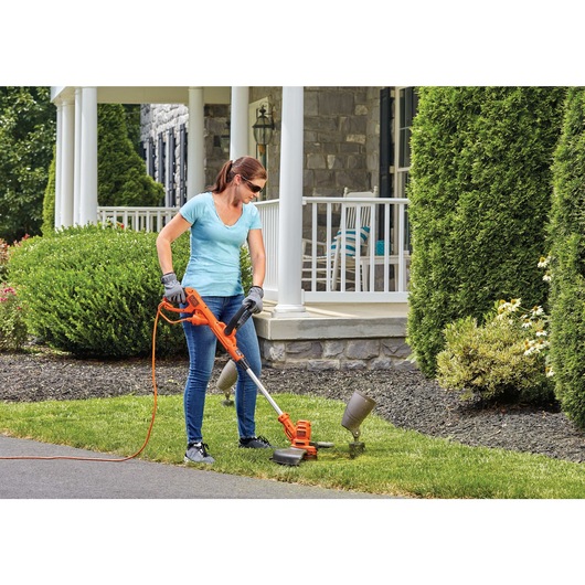 6.5 amp 14 inch a f s electric string trimmer and edger being used to trim grass around a garden decoration by a person in front of a house.