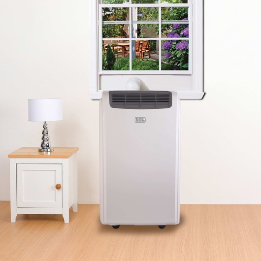 Portable Air Conditioner with remote control placed on floor in room with other furniture.