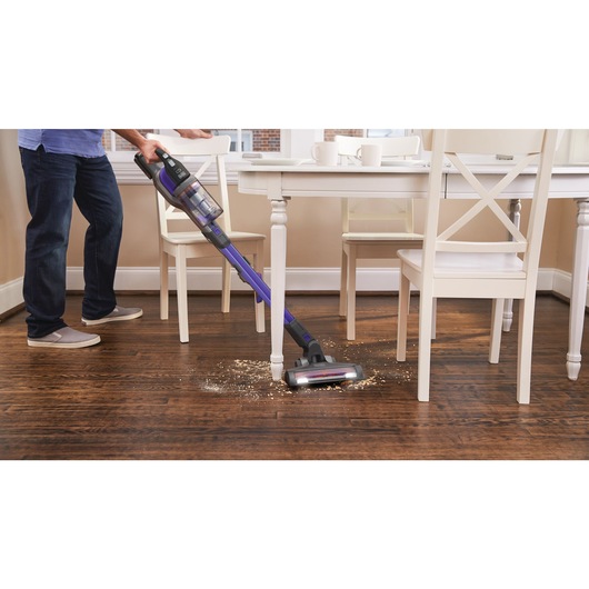 power series extreme pet cordless stick vacuum cleaner being used clean spilled material from the floor under a table.