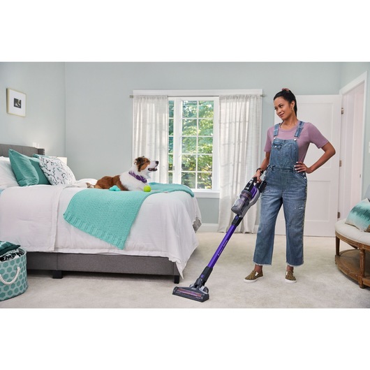 woman vacuuming bedroom carpet with BLACK+DECKER PowerseriesExtreme pet stick vacuum while dog is on the bed