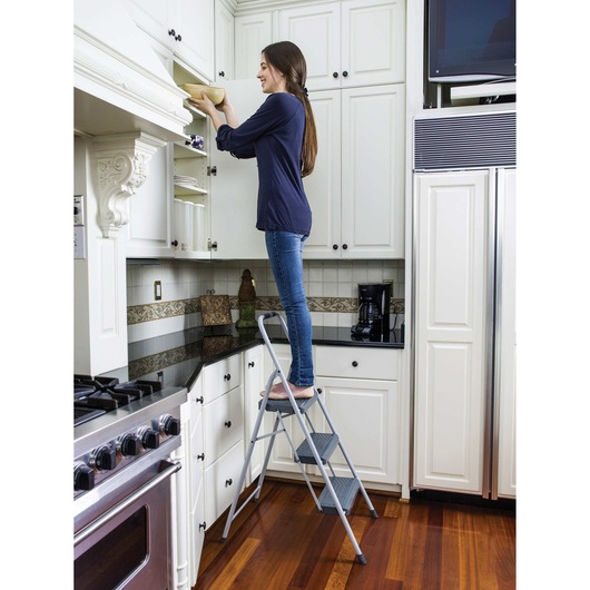 STEEL STEP STOOL 3 step Type II 225 pound load capacity being used by a person to reach cabinets.