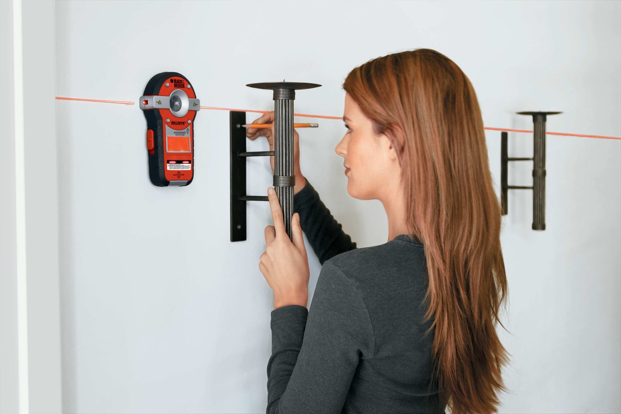 BullsEye Auto Leveling Laser with Stud Sensor being used by person to hang decorative items on wall.