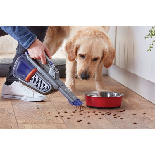 dustbuster AdvancedClean pet cordless hand vacuum being used by a person to clean dog food spillage on wooden floor.