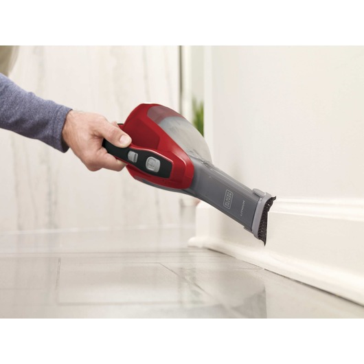 Dustbuster Advanced Clean Cordless Hand Vacuum with brush attachment being used to clean baseboard of wall.