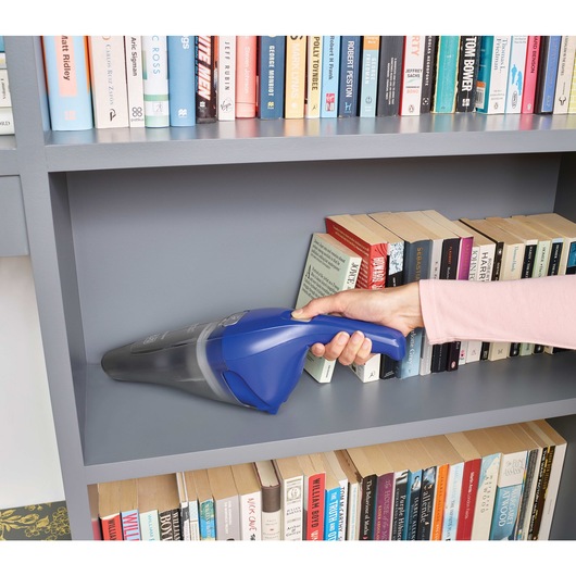 Dustbuster quickclean cordless hand vacuum being used to vacuum dust from the book shelves.