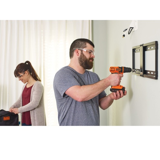 Lithium ion drill and driver being used by a person to drill a tv frame into the wall.