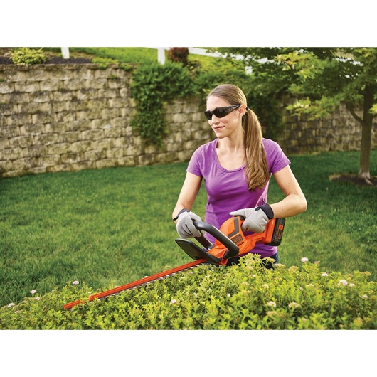 40 volt MAX 22 inch hedge trimmer being used by a person to trim hedge.