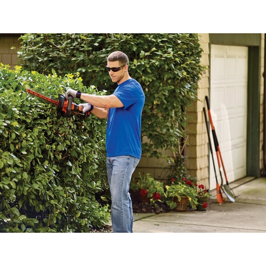 MAX Lithium 22 inch POWERCUT Hedge Trimmer being used by person to trim hedge outdoors.