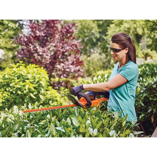 Lithium 22 inch power cut hedge trimmer being used to to trim a bush by a person.