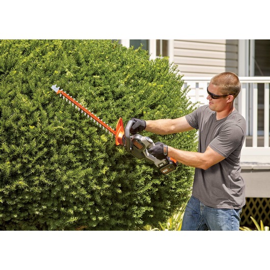 60 volt MAX POWER CUT 24 inch cordless hedge trimmer being used by a person to trim hedge.