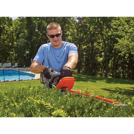 60 volt MAX POWER CUT 24 inch cordless hedge trimmer being used by a person to trim hedge.
