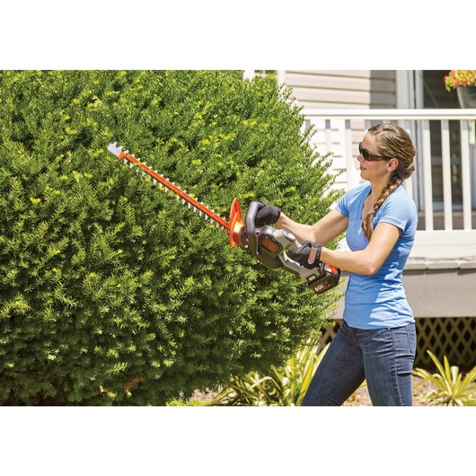 POWER CUT 24 inch Cordless Hedge Trimmer being used by person to trim bushes.