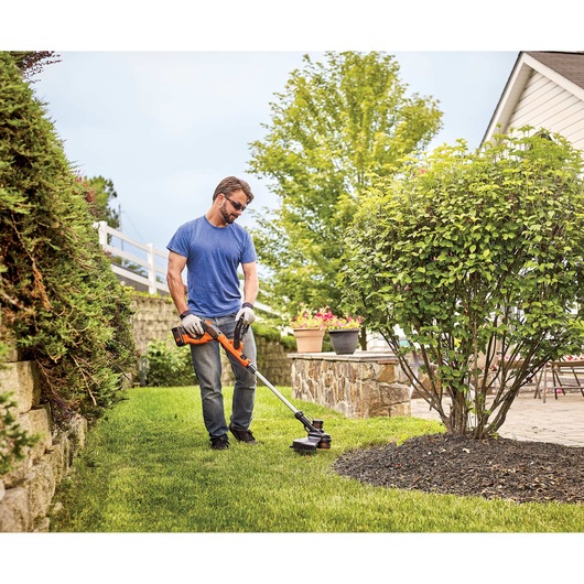 MAX Lithium String Trimmer being used by person to define edges around trenched tree outdoors.