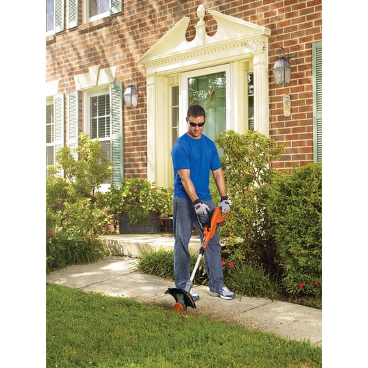 Lithium 12 inch trimmer and edger being used to trim the edge of a path by a person.