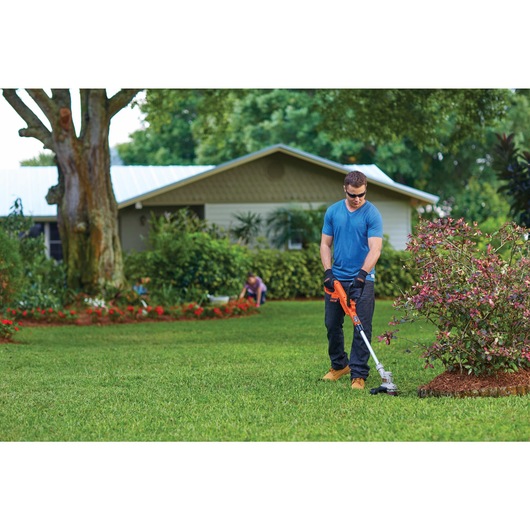 Lithium 12 inch Trimmer Edger being used by person to trim grass in garden beside house.