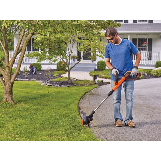 20 volt MAX Lithium 12 inch Trimmer / Edger being used on the ground outdoor by a person.