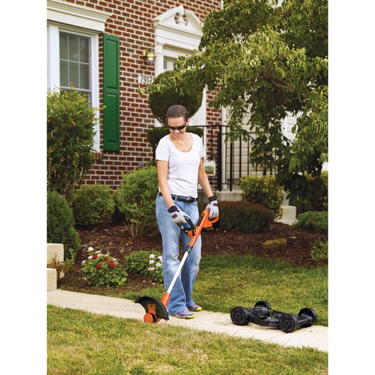 20 volt MAX Lithium 12 inch 3 in 1 Compact Mower being used on the lawn outside by a person.