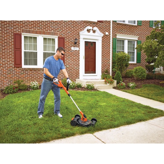 20 volt MAX lithium 12 inch 3 in 1 compact mower being used by a person to trim grass.