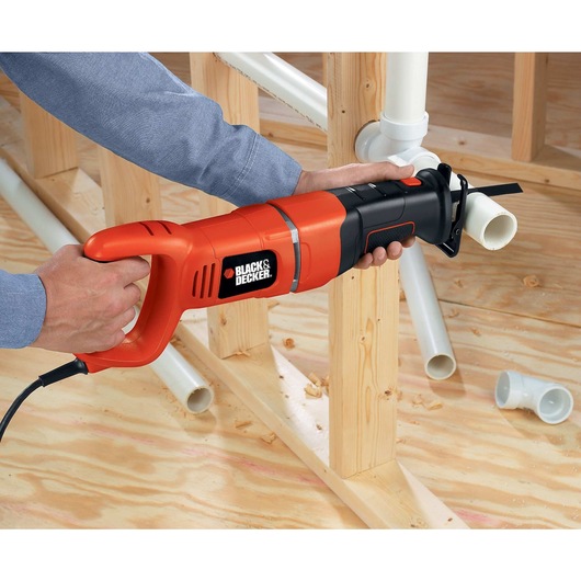Black and decker saber saw being used by a person to cut a plastic pipe indoors.