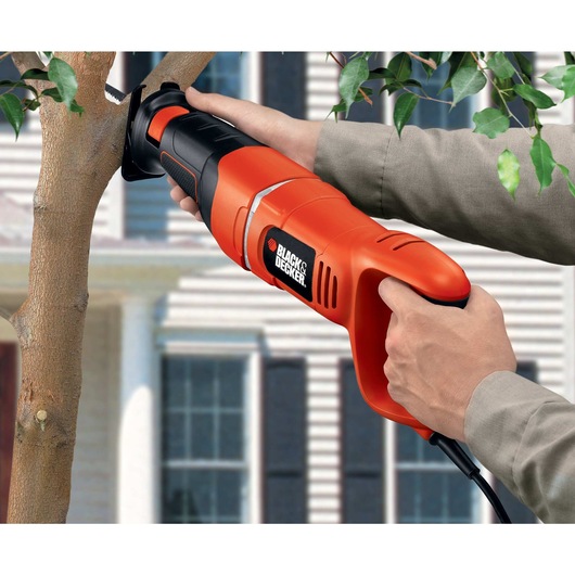 Black and decker saber saw being used by a person to cut a wood branch outdoors.