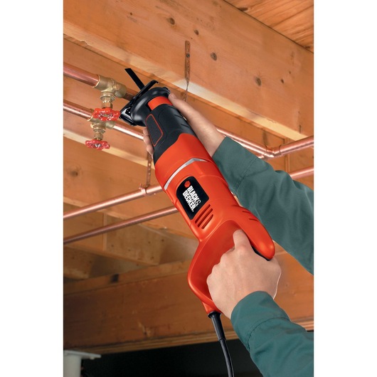 Black and decker saber saw being used by a person to cut through metal pipe near the roof indoors.