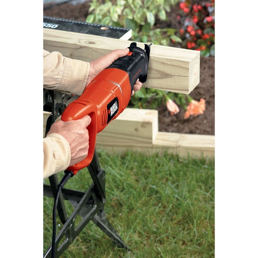 Black and decker saber saw being used by a person to cut through wood outdoors.