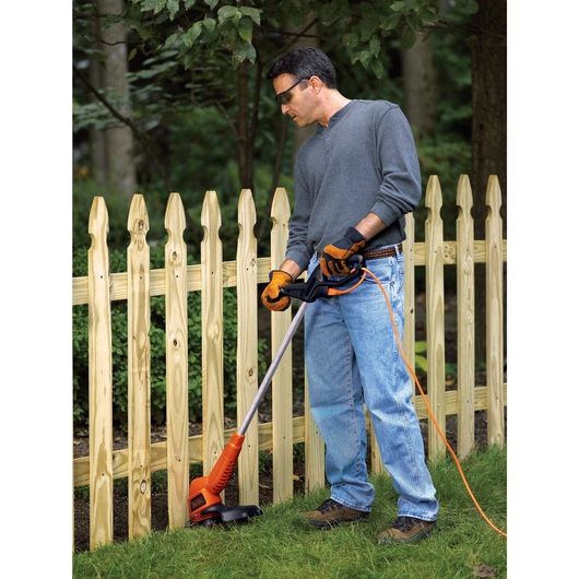 2 in 1 Trimmer and Edger being used to trim grass near fence by person.